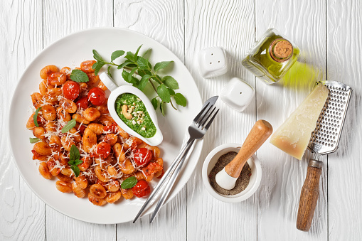 Potato gnocchi italian dish with cherry tomatoes and parmesan cheese on a white plate with pesto of cashew nuts mint, basil, and spinach on a white wooden background, top view, horizontal, close-up