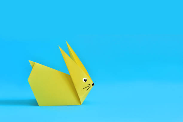 Two colorful origami Easter bunny rabbits made of paper in green and blue, of different sizes, perhaps parent and baby standing side by side, ready for Easter, isolated on white background