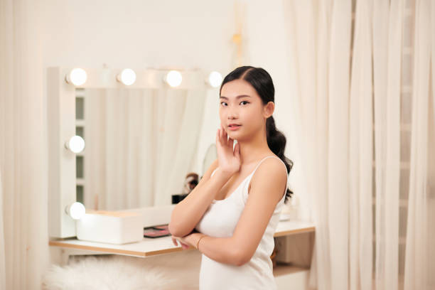 istock Taking off her make-up. Beautiful cheerful young woman using cotton disk and looking at her reflection in mirror with smile while sitting at the dressing table 1307883209