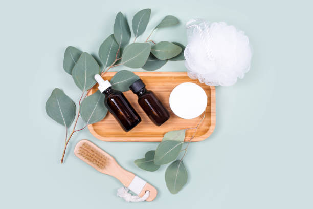 istock Essential oils, facial creme container and massage brushes with natural eucalyptus leaves on green background. Beauty products, massage tools, facial skin care, spa beauty treatment concept. Flat lay 1307883691