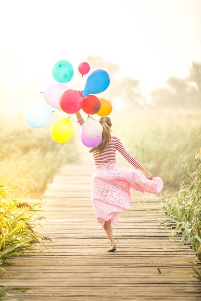 Stylish girl 4-5 years old holding a balloon in a trendy white dress on the meadow. Birthday.