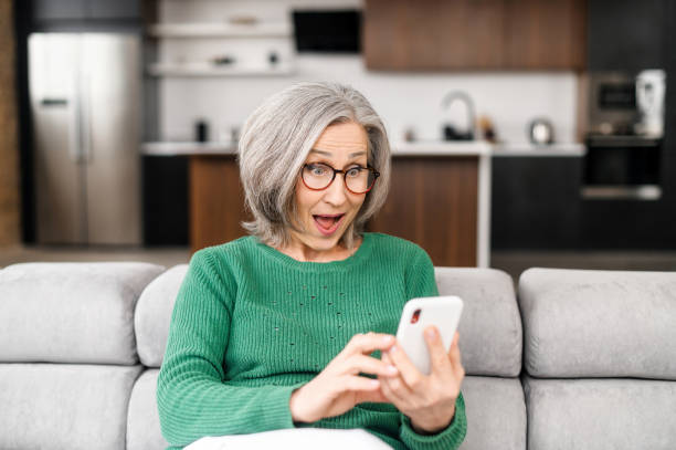 donna anziana matura che usa uno smartphone a casa - shock grandmother surprise senior adult foto e immagini stock