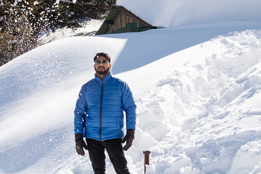 Handsome man in warm clothing and sunglasses standing on snowcapped mountain