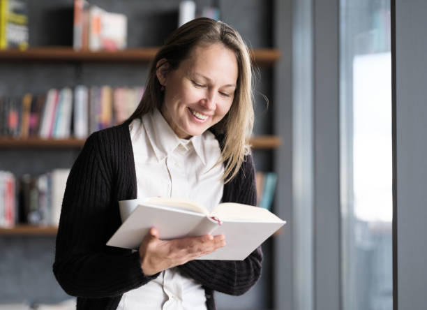 istock Young Woman Reading Book Nearby Window 1307896674