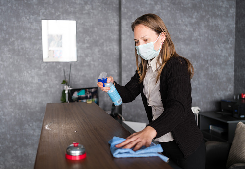 Receptionist Cleaning Desk With Disinfectant At Reception