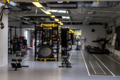 Photo of a blur gym background fitness center or health club with blurry sports exercise equipment for aerobic workout and bodybuilding. Gym background blurred. Blurred gym interior space background.