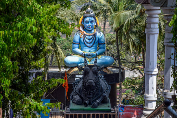 Front view of giant blue color statue of lord shiva and his vehicle nandi bull under bright sunlight surrounded by green trees at kanheri math kolhapur city maharashtra India. focus on statue. Front view of giant blue color statue of lord shiva and his vehicle nandi bull under bright sunlight surrounded by green trees at kanheri math kolhapur city maharashtra India. focus on statue. kolhapur stock pictures, royalty-free photos & images