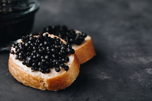 Black caviar sandwiches with butter on dark concrete background