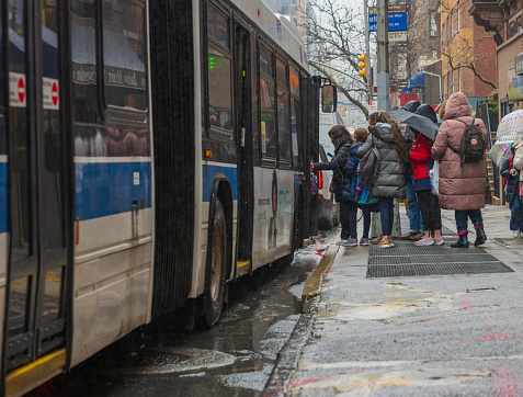 New York, NY, USA - March 18, 2021: People board bus in the rain on a chilly afternoon on Lexington Avenue in the Carnegie Hill section of Manhattan's upper east side.
