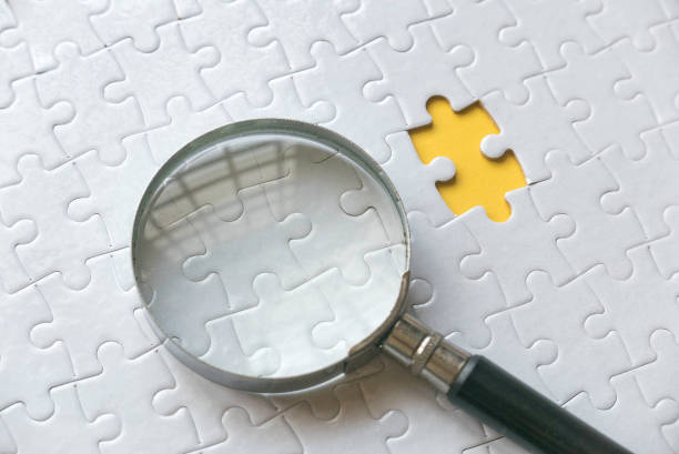 istock Selective focus of magnifying glass cone and an empty space of white jigsaw puzzle with yellow background. 1307907367