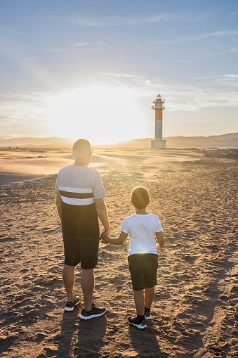 Grandfather and grandson hugging on a beach with a lighthouse in the background