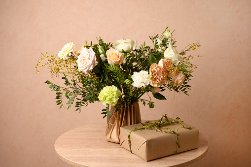 Beautiful flowers in vase and gift box on a table with beige background. Women's, mother's day, love concept. Spring, summer season. Front view.