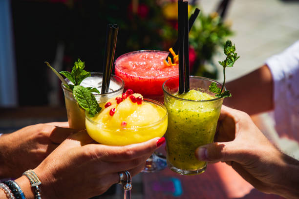Four hands holding glasses with yellow and red fruit cocktails in a toast Four hands holding drinking glasses with yellow and red fruit cocktails, proposing a toast at outdoor party mango fruit photos stock pictures, royalty-free photos & images