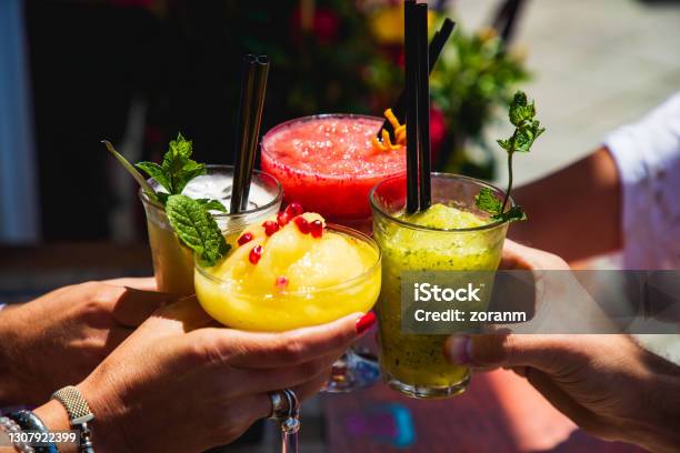 Four Hands Holding Glasses With Yellow And Red Fruit Cocktails In A Toast Stock Photo - Download Image Now