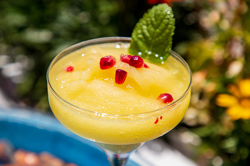 Close-up on pineapple cocktail in glass with pomegranate see and mint leaf decoration