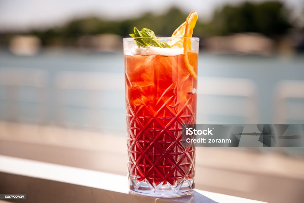 Red cocktail on the rocks with mint leaf and orange peal Punch on the rocks in drinking glass decorated with mint leaf and orange peal, outdoor bar Punch - Drink Stock Photo