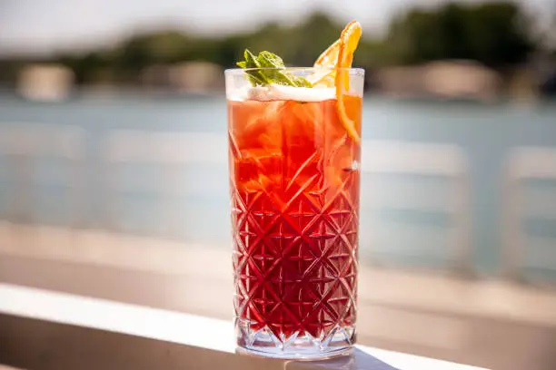 Punch on the rocks in drinking glass decorated with mint leaf and orange peal, outdoor bar