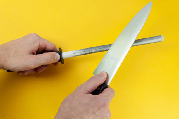 istock Man hand sharpenes knife on yellow background. Knife sharpening using a knife grinder. 1307923864