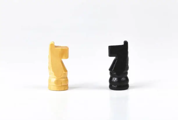 Two simple black and white knight, horse chess pieces opposing, facing each other, face to face, two sides business battle, confrontation and strategy, enemies and opponents tension abstract concept