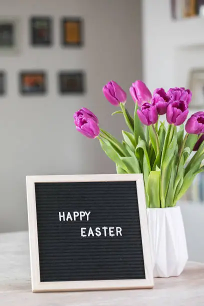 Spring concept. Bouquet of purple tulips flowers and letter board with the words Happy Easter. Happy Easter greeting card, gift, poster, web concept.