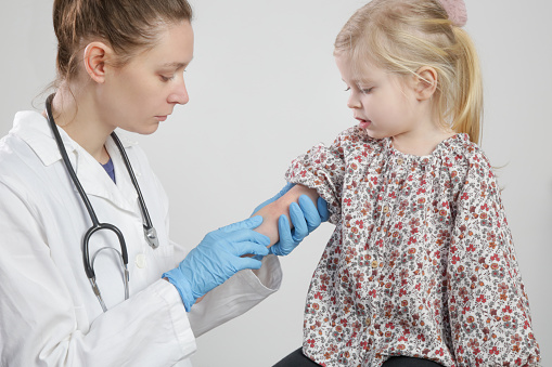 Doctor looking at red and itchy eczema on little girl's arm. Toddler girl suffering from atopic dermatitis.