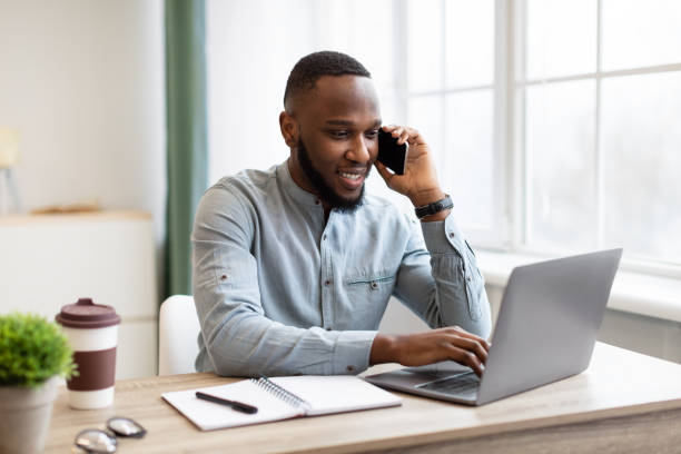 istock Happy African Business Guy Talking On Cellphone Sitting At Workplace 1307927756