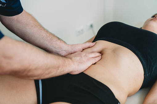 Chiropractor massaging the abdomen of a young adult woman. They are in a medical clinic.
