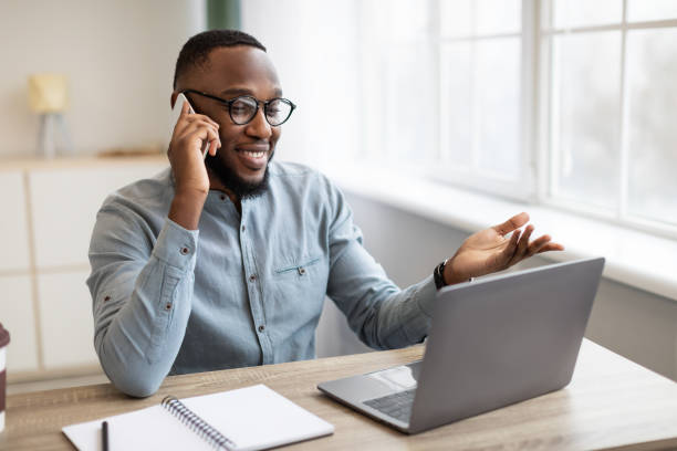 istock Black Businessman Talking On Phone Sitting At Workplace In Office 1307928478