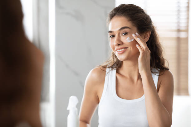 istock Happy Woman Applying Face Cream Standing In Modern Bathroom 1307929135