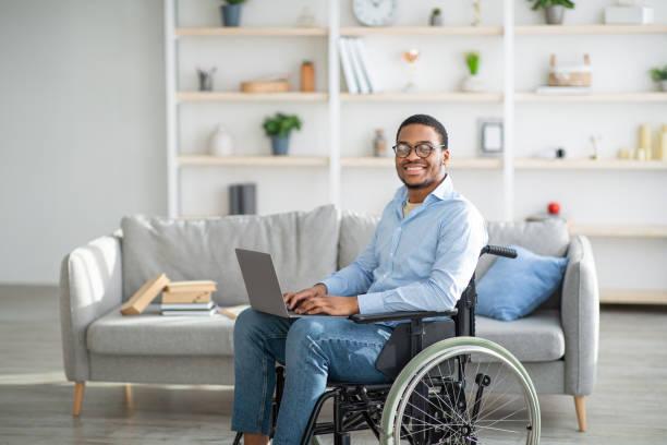istock Happy disabled black man in wheelchair using laptop, working online from home, copy space 1307929595