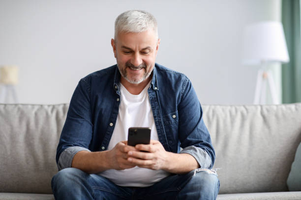 istock Smiling mature grey-haired man using mobile phone at home 1307932763