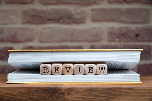 Review word written on wooden blocks between book pages on a shelf.