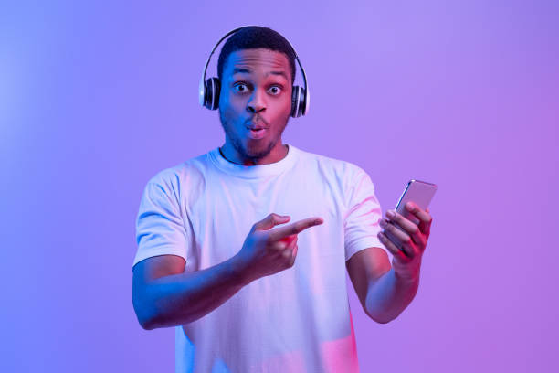 istock Cool App. Surprised Black Guy In Wireless Headphones Pointing At Smartphone 1307933524
