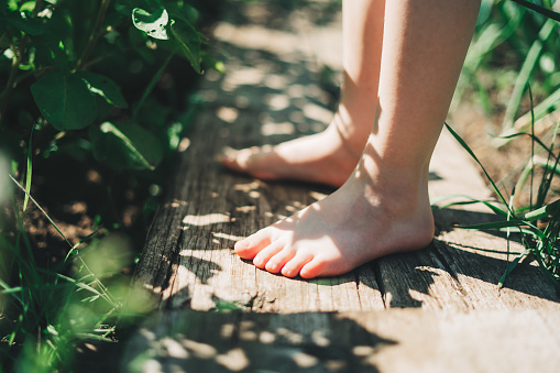Kid walking barefoot on wood plank at a grass field. Close up feet. Detail of kids legs walking on wooden pathway barefoot. Playful child on a garden.