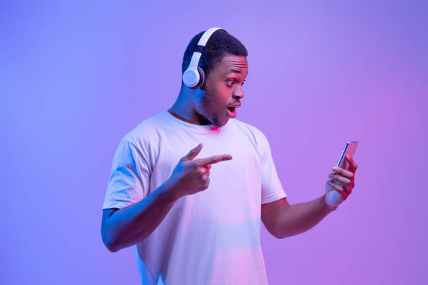 istock Amazed Black Guy In Wireless Headphones Pointing At Smartphone In His Hands 1307935015