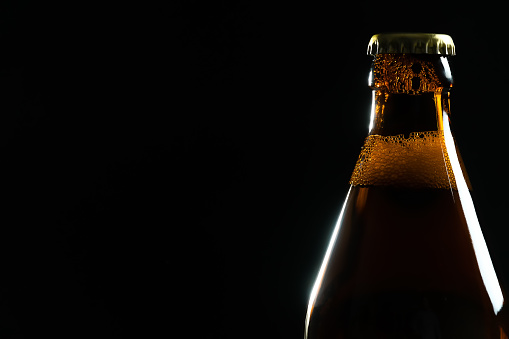 Sparkling beer in a glass. Little head on top of tall beer glass surrounded with two unopened brown bottles. Vertical still life on grey background.