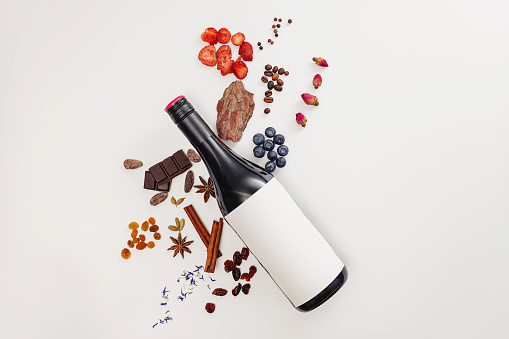 Creative composition with wine bottle and possible flavor components of red wine - berries, spices and other. Flat lay composition, wine tasting concept.