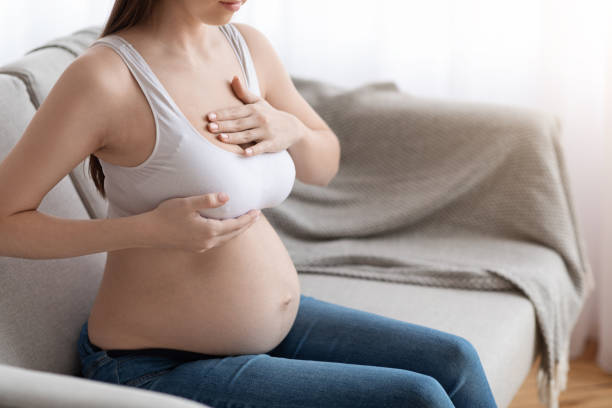 istock Unrecognizable pregnant lady massaging her breasts while sitting on couch at home 1307937851