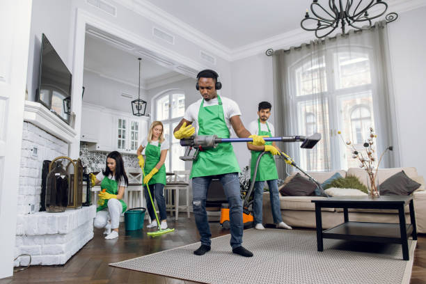 istock Young handsome crazy black-skinned cleaning service man in uniform, having fun wearing headphones, listening to music and dancing with vacuum cleaner. His colleagues tidying customer house 1307938796