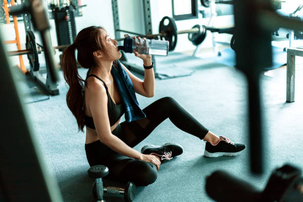 istock woman taking a break and  drinking water after workout at gym. 1307940153