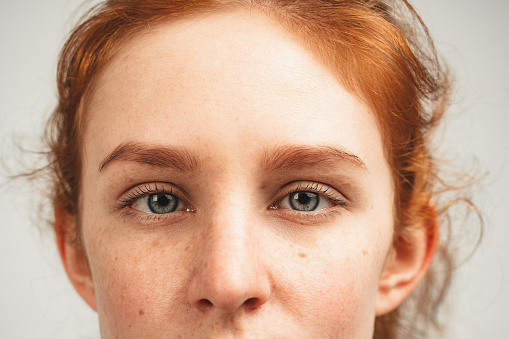 Close up face of young woman with blue eyes natural redhead watch at camera. Isolated over white background. Natural beauty and health.