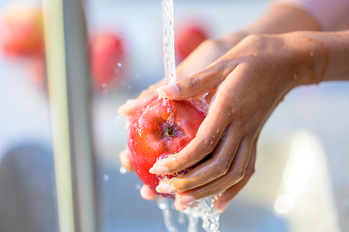 Woman washing red apple in running water. Cropped view on female hands holding fruit in water stream. Healthy eating, fruits and vitamins concept.