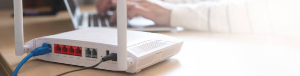 istock Banner horizontal shot of Internet router on working table with blurred man connect the cable at the background. Fast and high speed internet connection from fiber line with LAN cable connection. 1307947999
