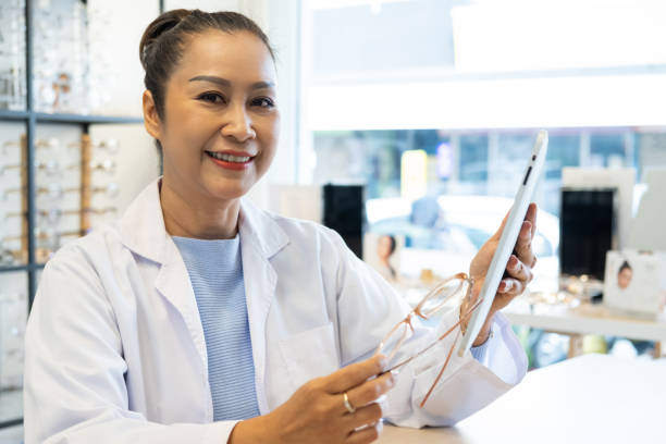 istock Asian women Doctor optometrist smiling while using tablet and recommend customer to choose glasses beautiful frame trial inside of optical shop, store. Eye sight for patient, healthcare concept. 1307948017