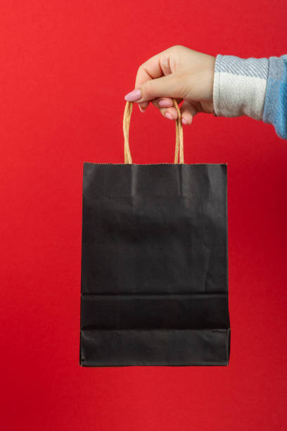 istock Black paper bag in hand on a red background. 1307950475