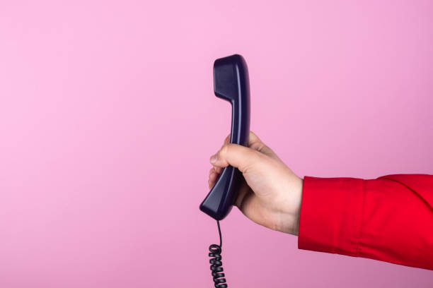 istock Hand holds a telephone receiver on a pink background. 1307950484