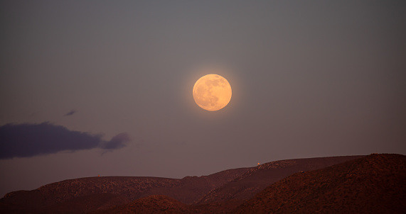 Full moon over barren landscape in Cabo de Gata red illuminated by sunset light Spain
