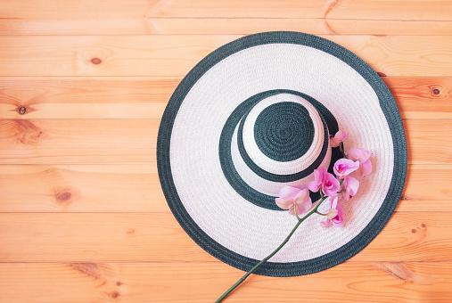 White summer hat  and purple orchid on wooden background. Summer and tropical holidays concept. Top view, copy space.