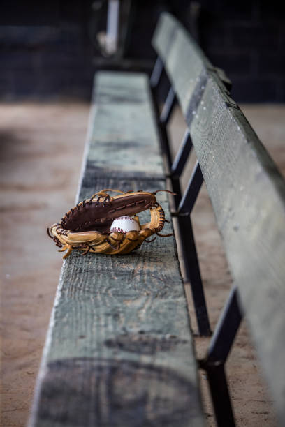 Empty dug out bench at a baseball field with a lone baseball glove and baseball sitting in the middle. Empty dug out bench at a baseball field with a lone baseball glove and baseball sitting in the middle.. The seating is covered in dust and pollen. baseball baseballs spring training professional sport stock pictures, royalty-free photos & images
