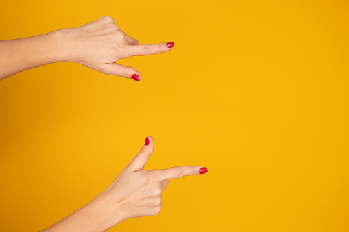 Female hands close-up, long index finger pointing at something. Gesture of direction. Yellow background. Copy space. Hand sign concept. High quality photo